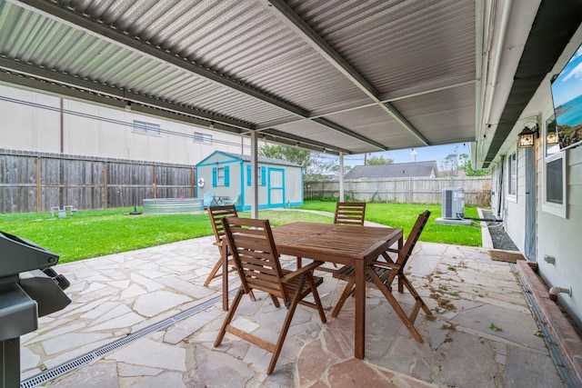 view of patio featuring central AC, outdoor dining area, a fenced backyard, a storage shed, and an outbuilding