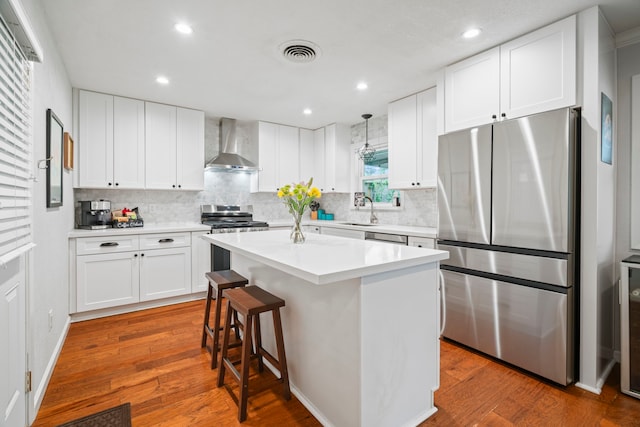 kitchen with wall chimney range hood, visible vents, appliances with stainless steel finishes, tasteful backsplash, and a sink