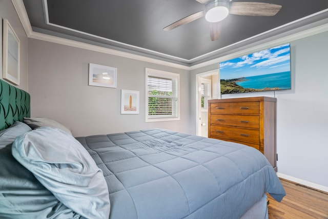 bedroom with crown molding, a ceiling fan, a tray ceiling, and wood finished floors
