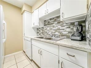 kitchen featuring decorative backsplash, light tile patterned flooring, white cabinets, white appliances, and a sink