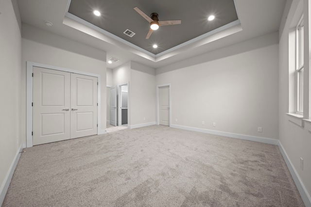 unfurnished bedroom with a tray ceiling, light carpet, baseboards, visible vents, and recessed lighting