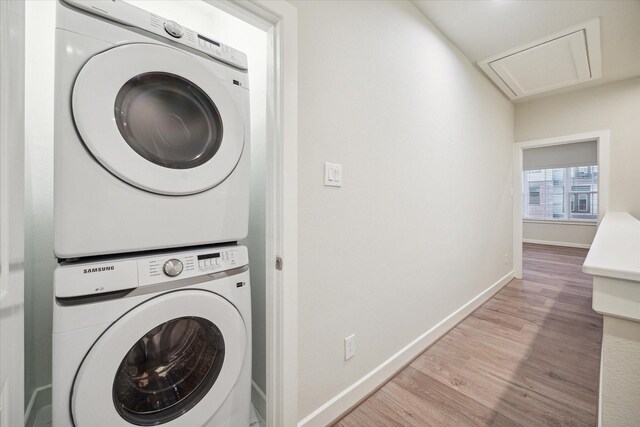 laundry area with light wood finished floors, stacked washer and dryer, baseboards, and laundry area