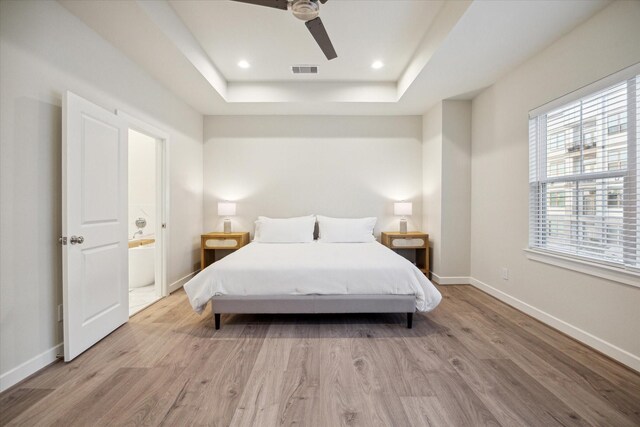 bedroom featuring a tray ceiling, wood finished floors, baseboards, visible vents, and recessed lighting