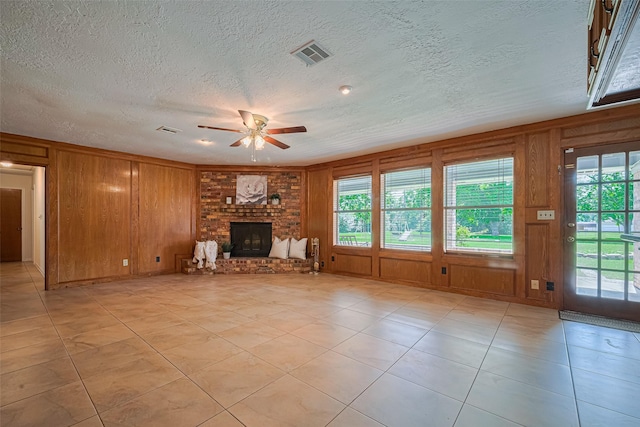 26003 Fountaine Bleau Dr, Tomball, TX 77377 - unfurnished living room featuring ceiling fan, a fireplace, a textured ceiling, wood walls, and light tile patterned floors