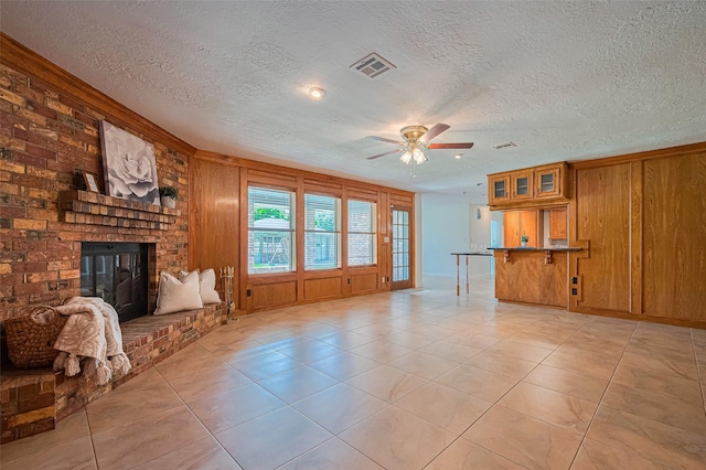 26003 Fountaine Bleau Dr, Tomball, TX 77377 - unfurnished living room featuring ceiling fan, a textured ceiling, a brick fireplace, light tile patterned floors, and wood walls