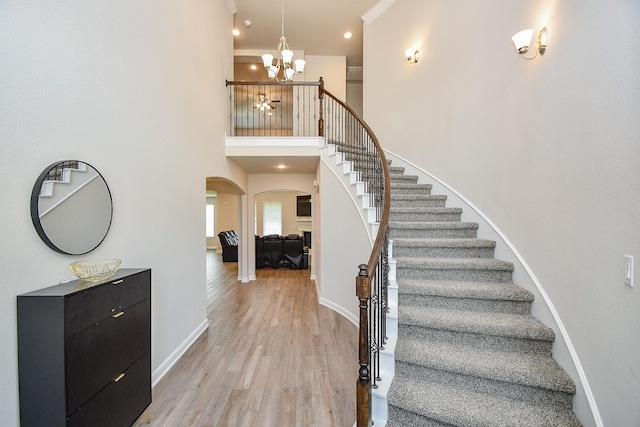 staircase with a towering ceiling, a notable chandelier, baseboards, arched walkways, and wood finished floors