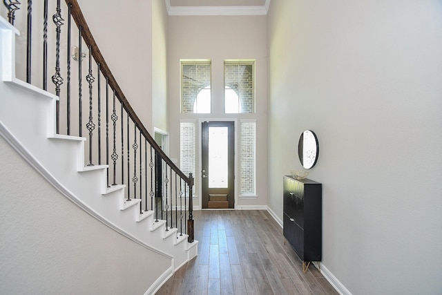 entrance foyer with baseboards, crown molding, wood finished floors, a towering ceiling, and stairs