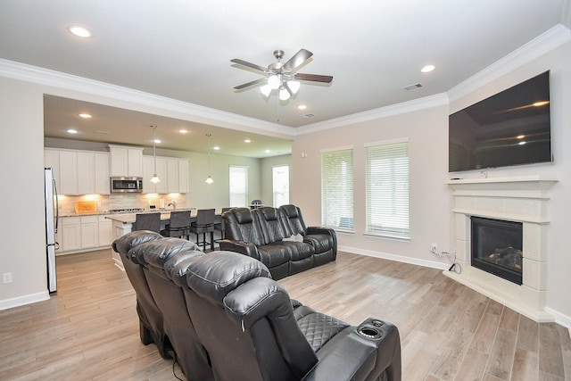 living room featuring light wood finished floors, visible vents, crown molding, and a ceiling fan