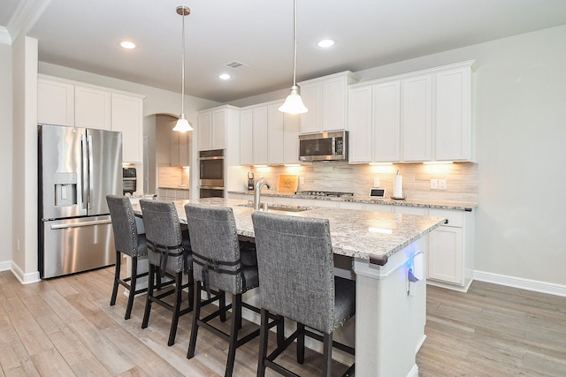 kitchen with light wood finished floors, appliances with stainless steel finishes, decorative backsplash, and a sink