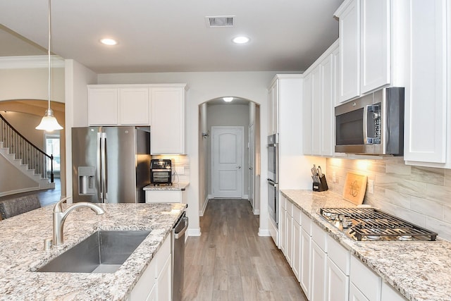 kitchen with white cabinets, visible vents, stainless steel appliances, arched walkways, and a sink