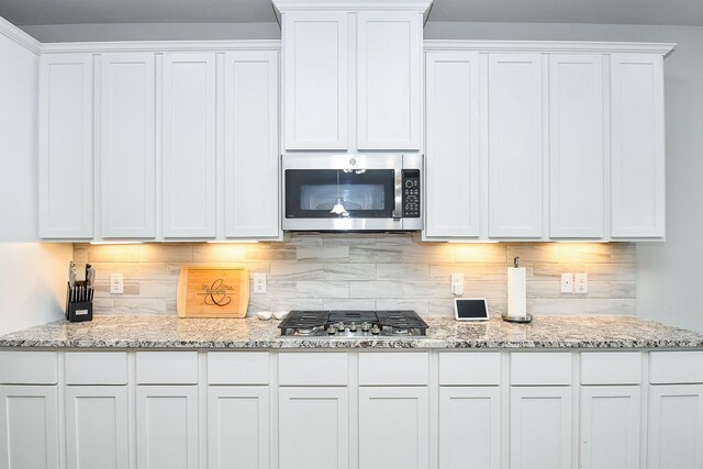 kitchen with backsplash, light stone countertops, white cabinetry, and stainless steel appliances