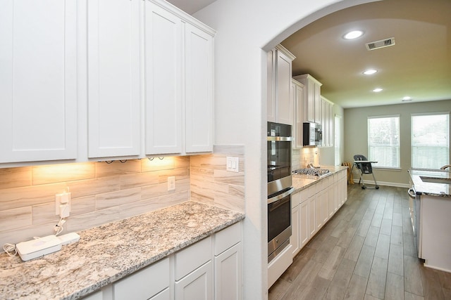 kitchen with arched walkways, white cabinetry, visible vents, a sink, and stainless steel appliances