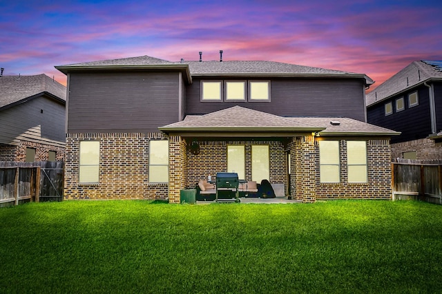back of house at dusk featuring a yard, a fenced backyard, and a patio