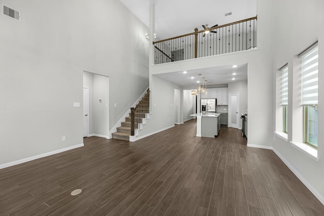 unfurnished living room featuring stairs, dark wood finished floors, baseboards, visible vents, and an inviting chandelier