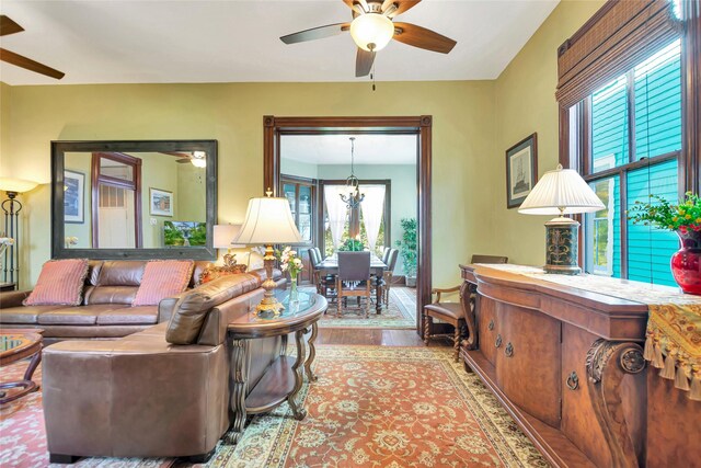 living area featuring ceiling fan with notable chandelier and wood finished floors