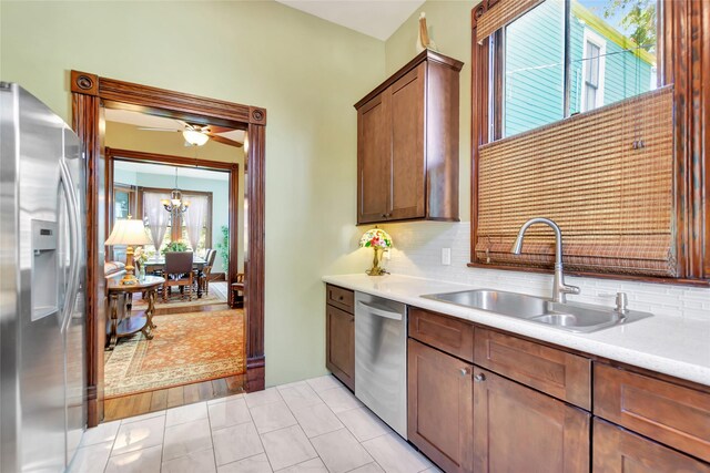 kitchen with light countertops, backsplash, a sink, stainless steel appliances, and ceiling fan with notable chandelier