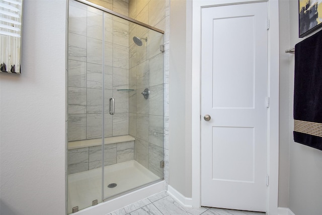 bathroom with marble finish floor, a stall shower, and baseboards