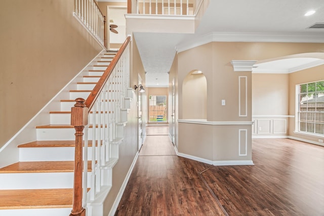 stairs featuring arched walkways, baseboards, wood finished floors, visible vents, and ornamental molding