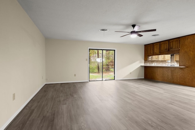 unfurnished living room with dark wood-style floors, visible vents, baseboards, and a ceiling fan