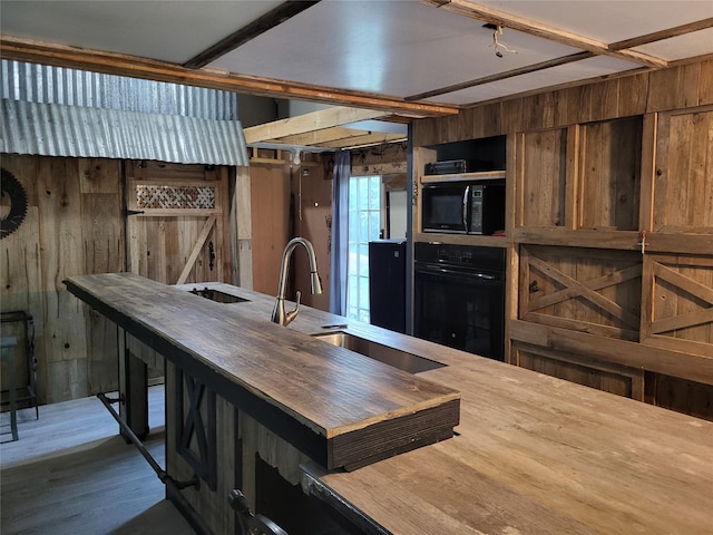 kitchen with wooden walls, black appliances, wood finished floors, and a sink