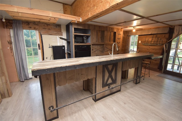 kitchen featuring wood counters, wooden walls, a kitchen breakfast bar, black appliances, and light wood-style floors