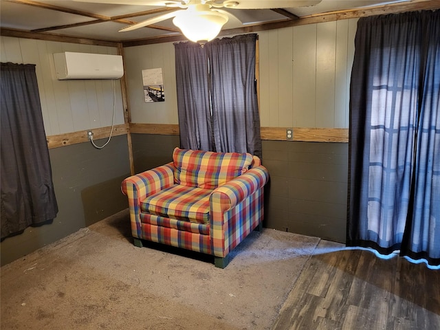 sitting room featuring wood finished floors, wooden walls, an AC wall unit, and a ceiling fan