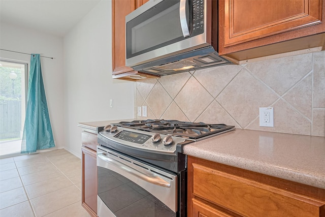 13600 Breton Ridge St Unit 22D, Houston, TX 77070 - kitchen featuring appliances with stainless steel finishes, brown cabinetry, tasteful backsplash, light tile patterned floors, and baseboards