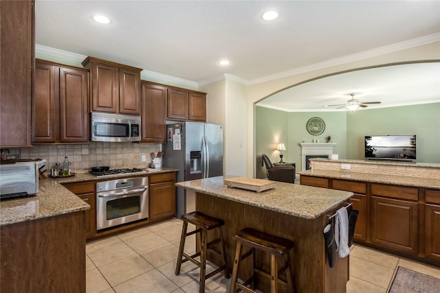 14711 E Ginger Spice Ct, Cypress, TX 77433 - kitchen with appliances with stainless steel finishes, a kitchen island, light tile patterned flooring, backsplash, and crown molding