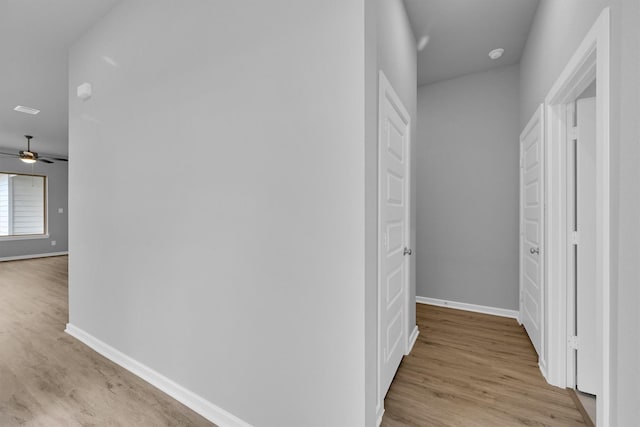 corridor with light wood-type flooring and baseboards