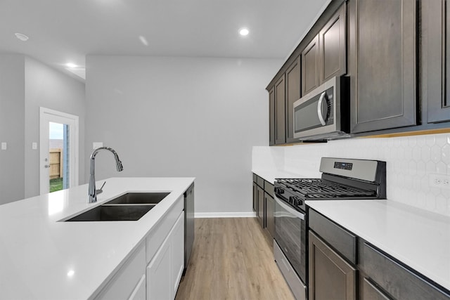 kitchen with tasteful backsplash, a sink, light countertops, light wood-type flooring, and stainless steel appliances