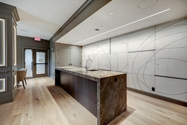kitchen with baseboards, a kitchen island with sink, light wood-style floors, and a sink