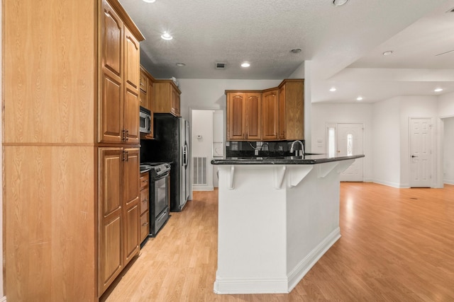 kitchen featuring a kitchen breakfast bar, visible vents, black electric range oven, stainless steel microwave, and a peninsula
