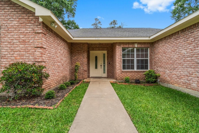 entrance to property featuring brick siding, roof with shingles, and a yard