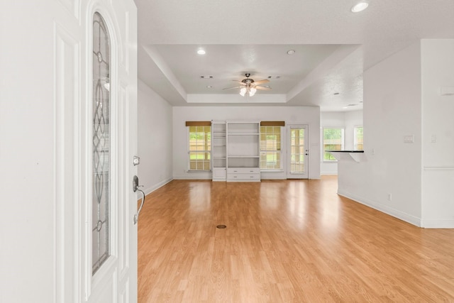 unfurnished living room featuring ceiling fan, a raised ceiling, baseboards, recessed lighting, and light wood-style flooring