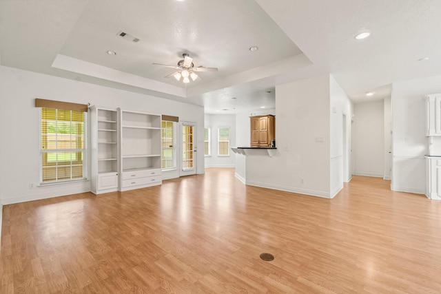 unfurnished living room with visible vents, ceiling fan, a tray ceiling, and a healthy amount of sunlight