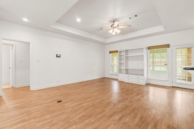 unfurnished room featuring a ceiling fan, a healthy amount of sunlight, a raised ceiling, and light wood-type flooring