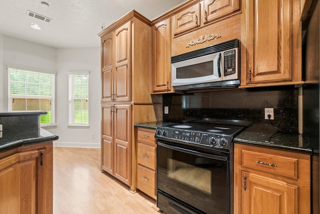 104 Mccardell Ln, Livingston, TX 77351 - kitchen with decorative backsplash, black range with electric cooktop, light wood-style floors, stainless steel microwave, and dark stone countertops
