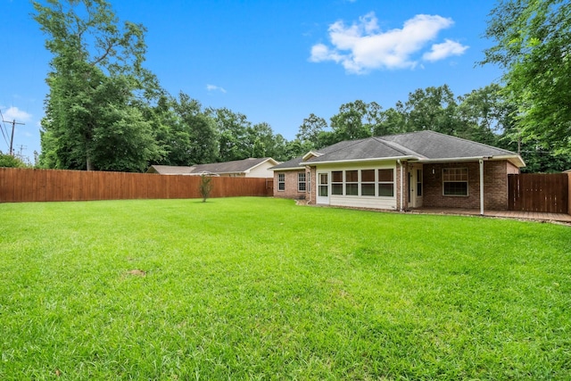 rear view of property featuring a lawn, brick siding, a fenced backyard, and a sunroom