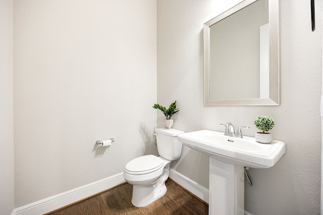 bathroom with baseboards, wood finished floors, toilet, and a sink