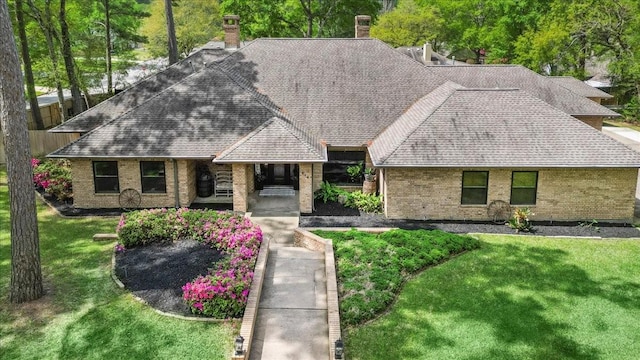 view of front of property with brick siding, a shingled roof, a front yard, and a chimney