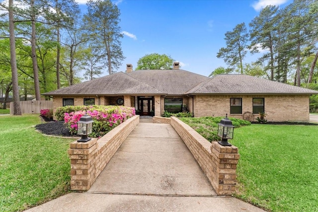 ranch-style house with brick siding, a chimney, a shingled roof, and a front yard
