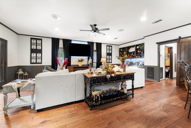 living area featuring visible vents, ornamental molding, wood finished floors, ceiling fan, and a barn door