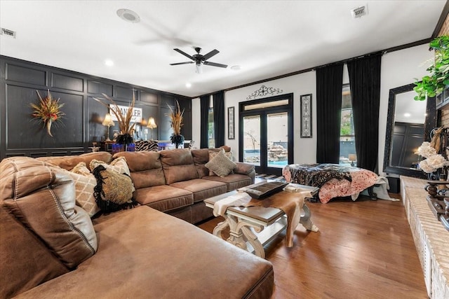 living area with crown molding, ceiling fan, a decorative wall, wood finished floors, and visible vents