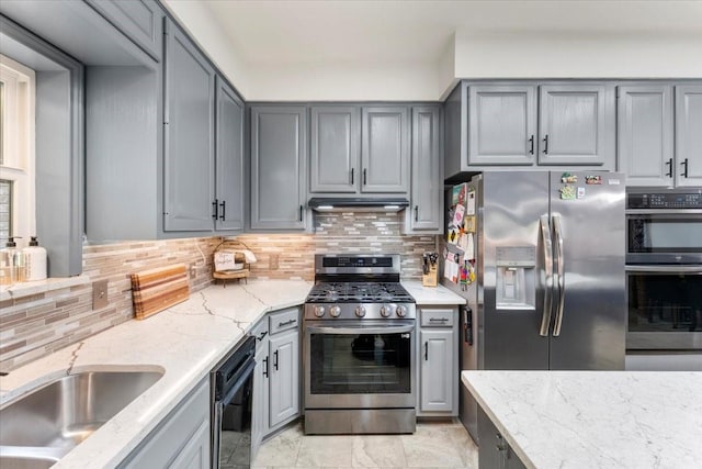 kitchen featuring under cabinet range hood, stainless steel appliances, gray cabinetry, and decorative backsplash