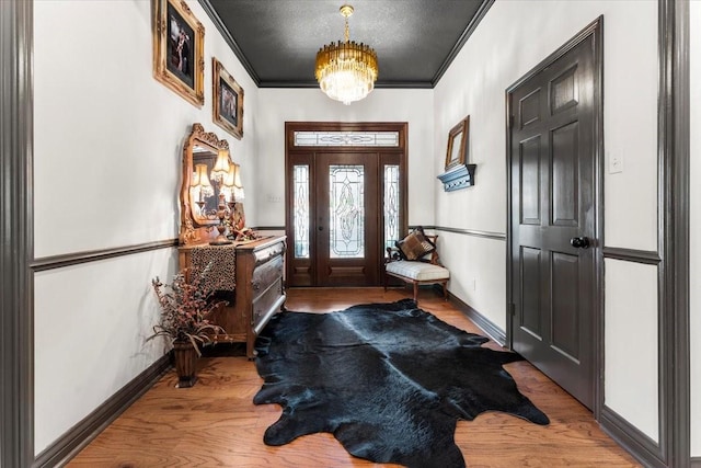 foyer featuring an inviting chandelier, baseboards, crown molding, and wood finished floors