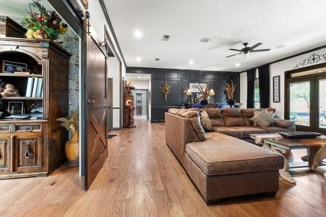 living room featuring ceiling fan, visible vents, crown molding, a barn door, and light wood-style floors