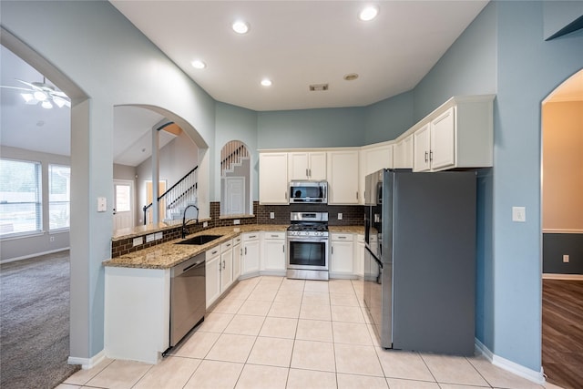 kitchen with baseboards, arched walkways, a sink, appliances with stainless steel finishes, and light stone countertops
