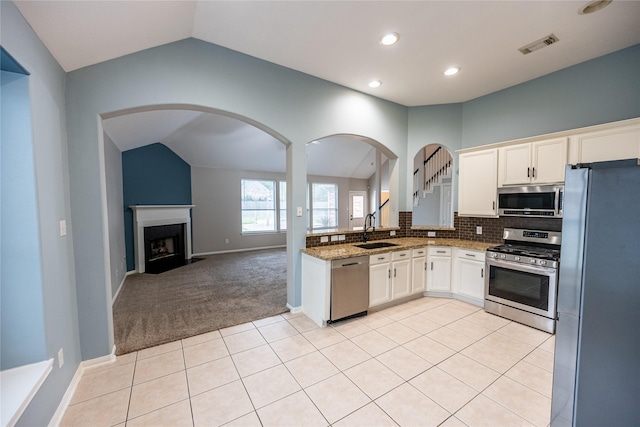 kitchen with white cabinets, stainless steel appliances, a sink, light stone countertops, and lofted ceiling