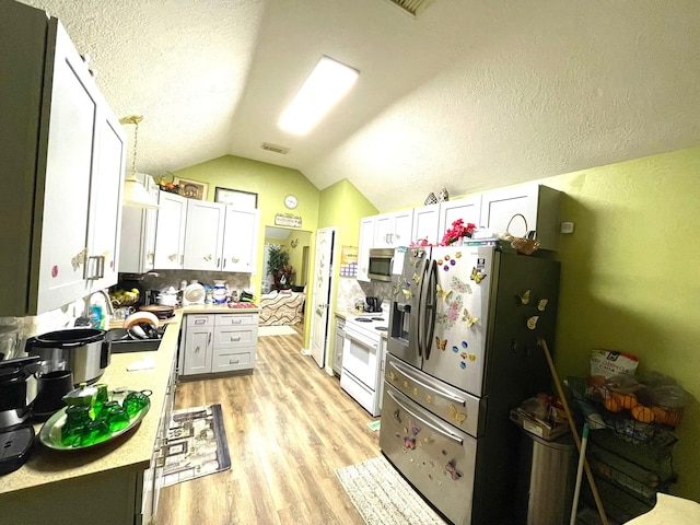 kitchen featuring light countertops, tasteful backsplash, lofted ceiling, light wood finished floors, and appliances with stainless steel finishes