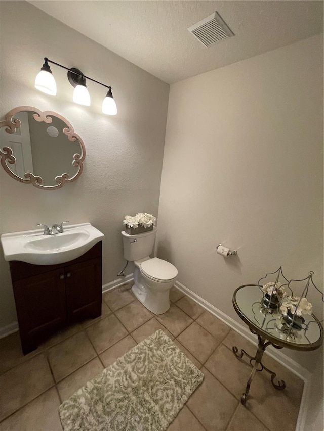 half bath featuring tile patterned flooring, toilet, vanity, baseboards, and visible vents